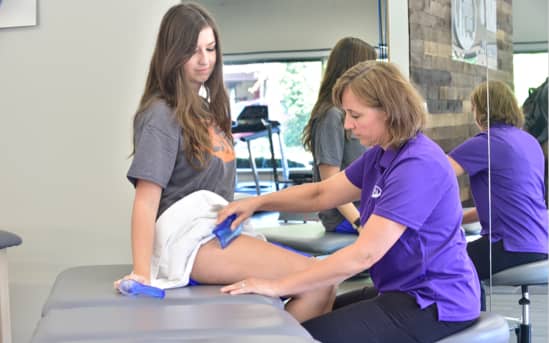 athletic trainer placing ice pack on young woman's leg