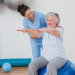 Happy instructor assisting senior woman in exercising at gym